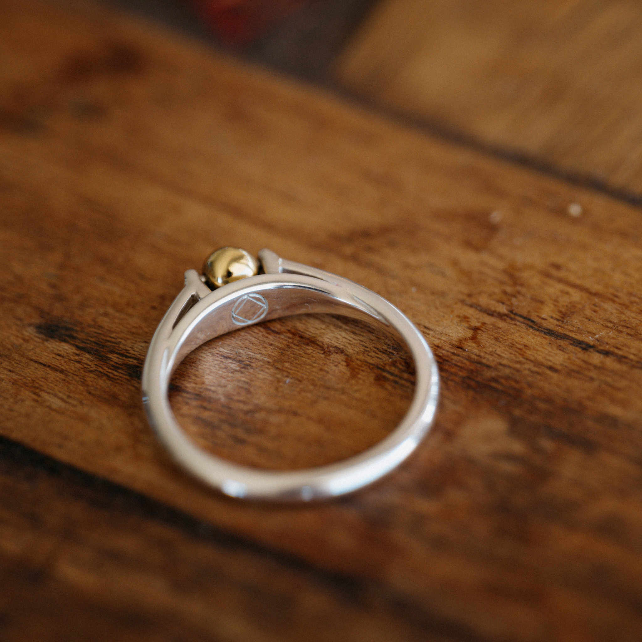 The India ring anxiety ring with silver band and mounted bronze ball placed on wooden table