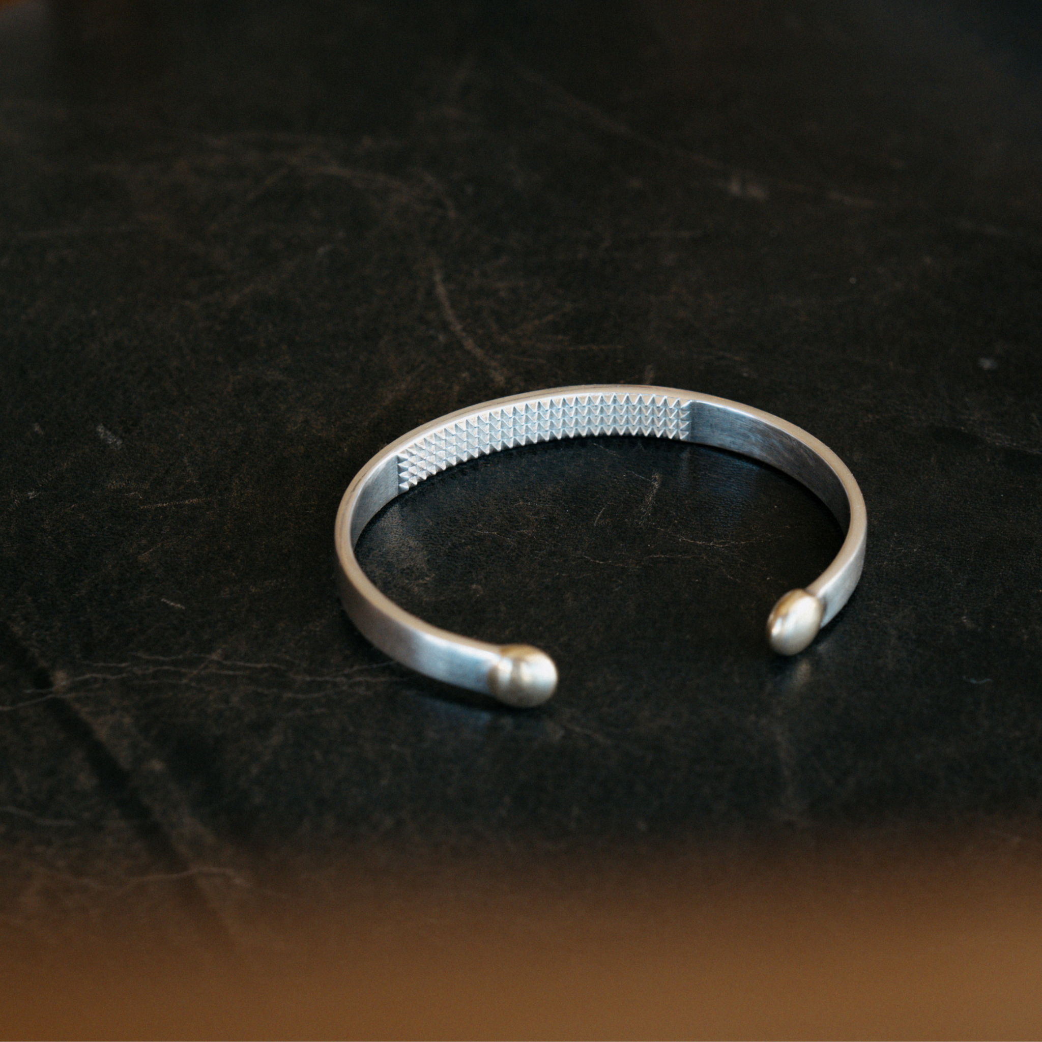 The Annika cuff anxiety bracelet in silver and bronze placed on dark coloured table