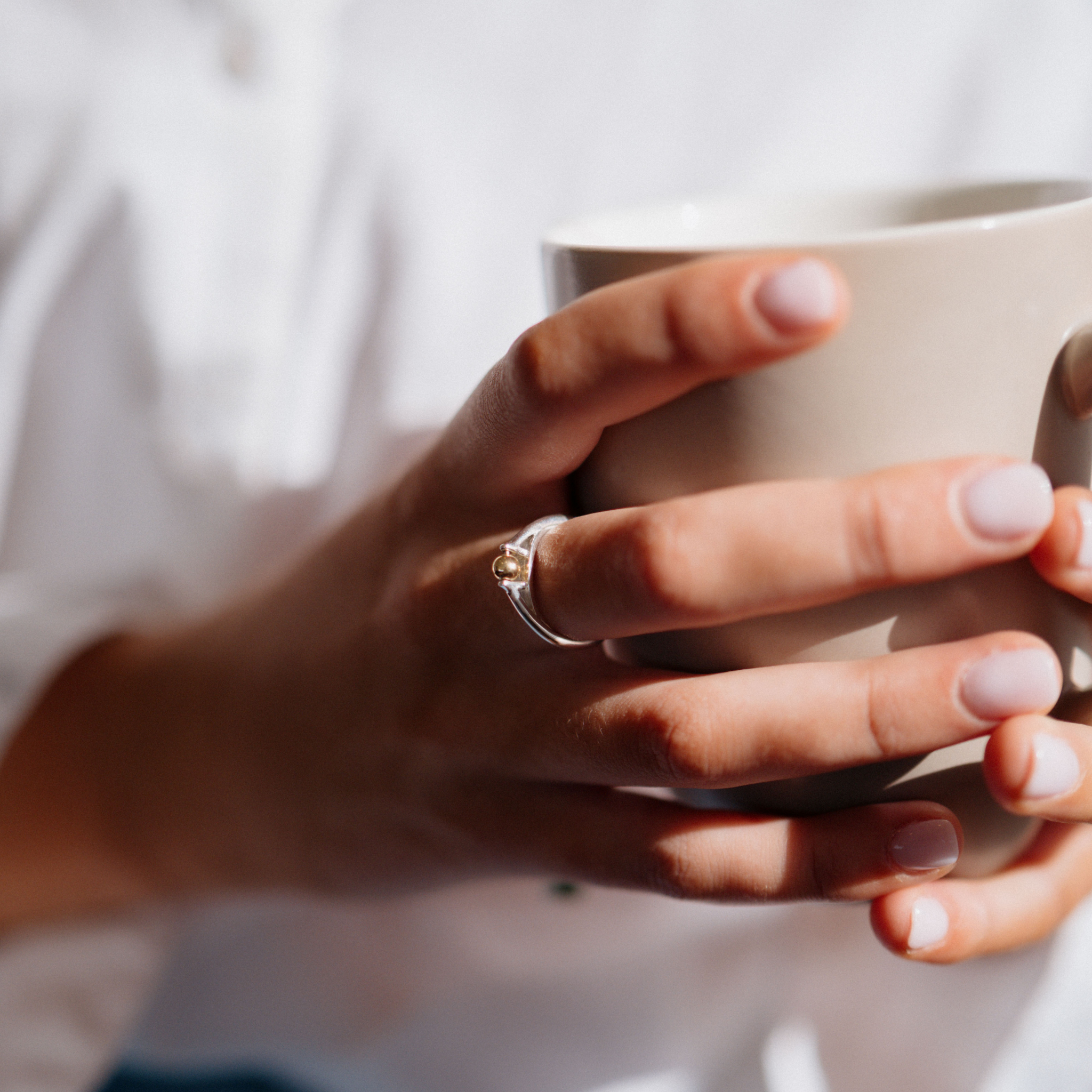 The India ring anxiety ring with silver band and mounted bronze ball being worn on girls hand whilst holding a mug